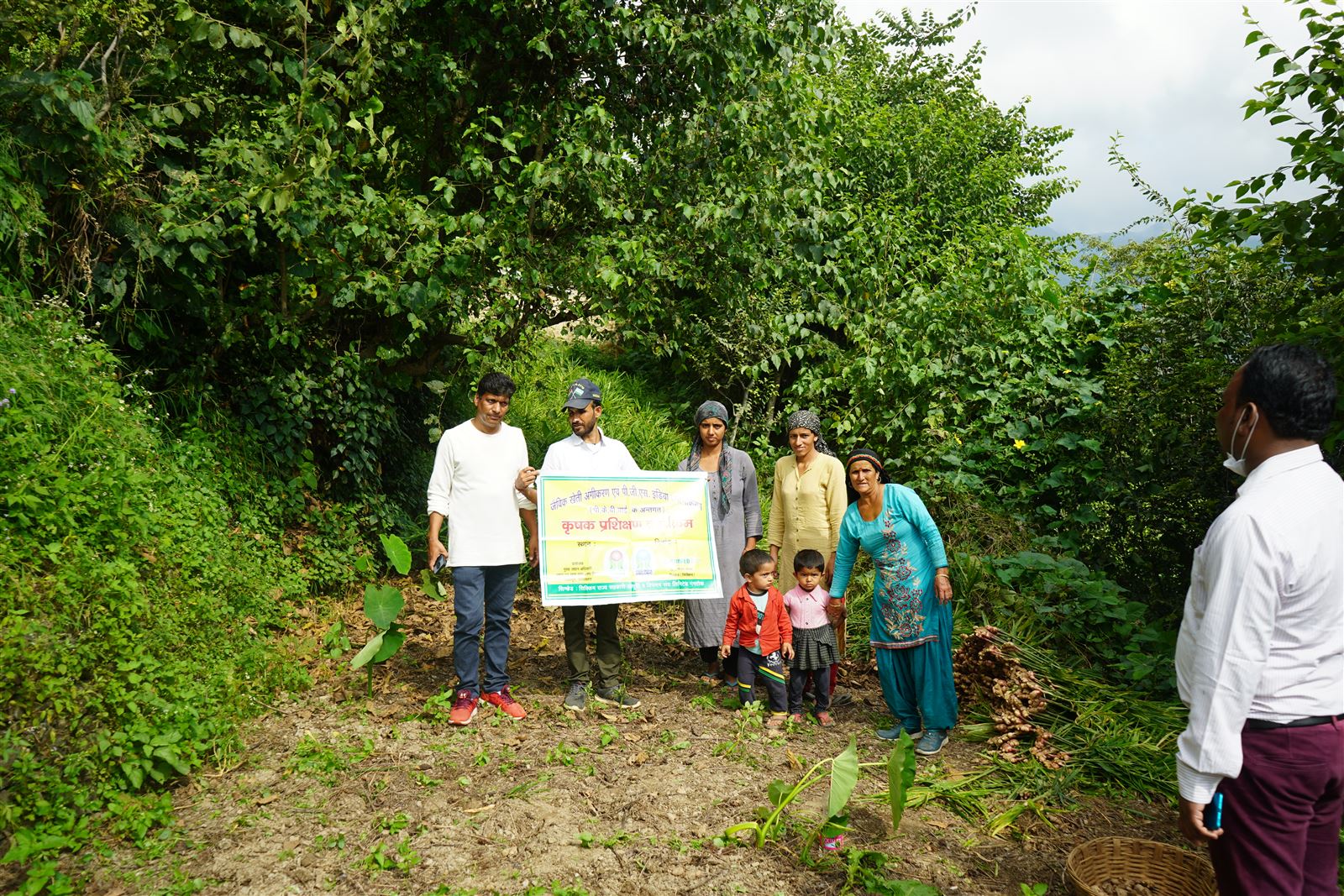 A group of farmers and staff standing with a project signboard on a hill path.