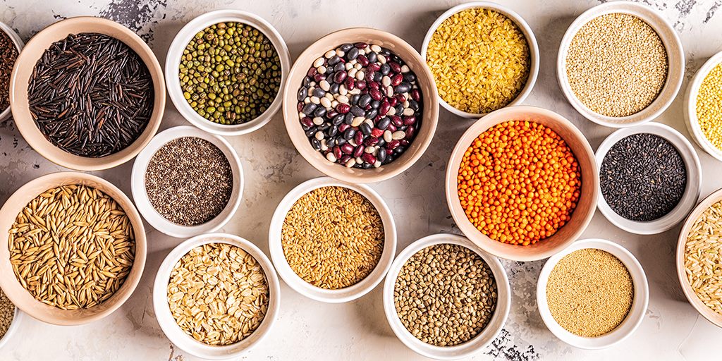 Bowls of assorted pulses, grains and spices arranged on a surface.